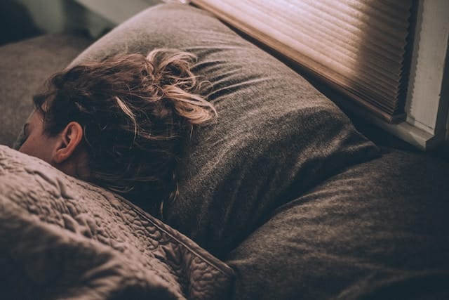 a person sleeping in bed, with sunlight coming through the blinds