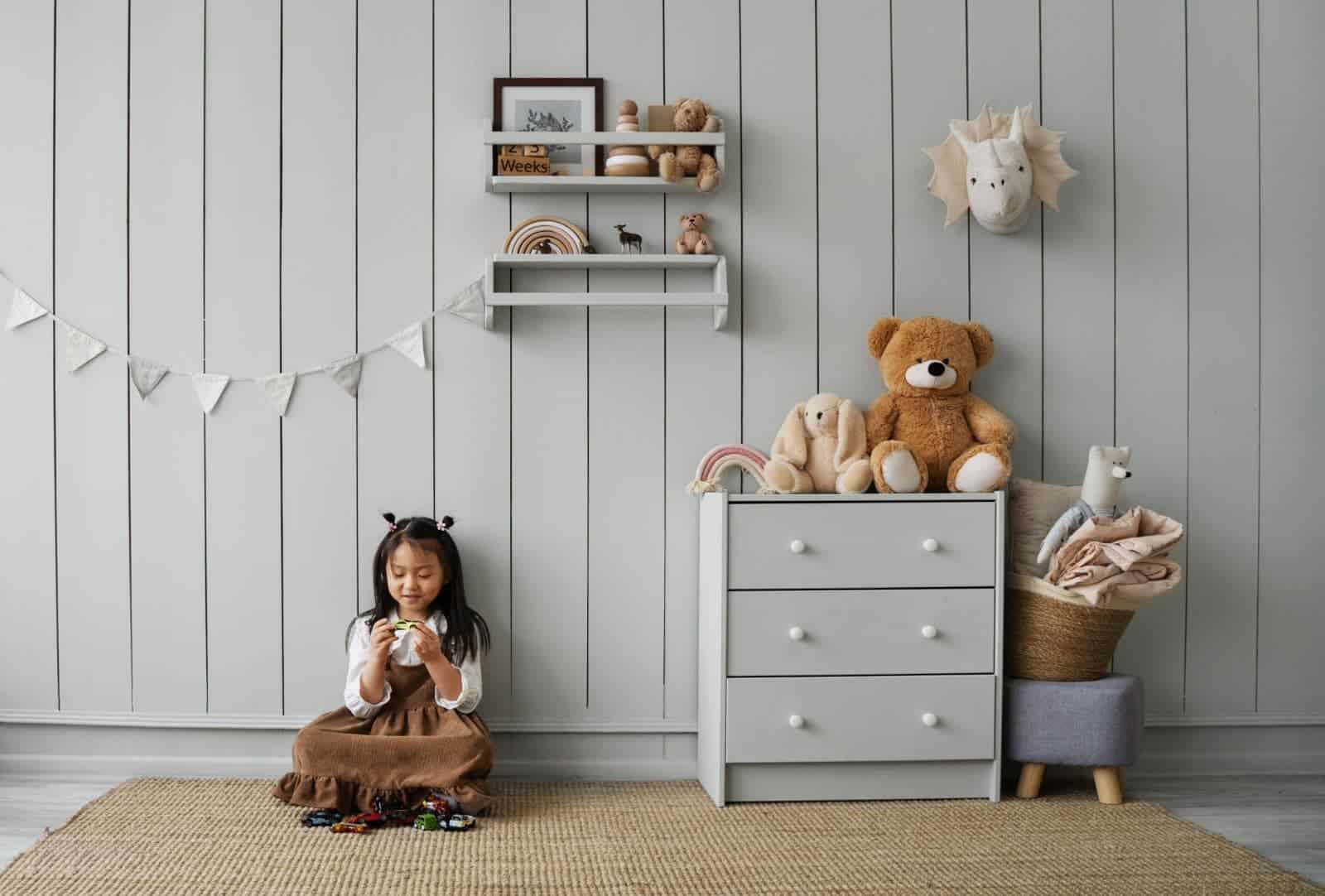 Young girl sitting on the floor of her tastefully decorated grey bedroom.