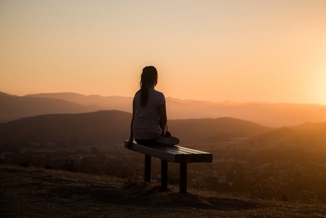 A woman on a bench, on top of a hill, looking out over a sunrise